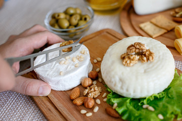 Chef slices the cheese. Cheese mix on a wooden plate decorated with grapes, nuts, salad and olives with cheese knifes 