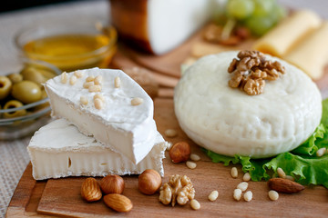 Cheese mix on a wooden plate decorated with grapes, nuts, salad and olives with cheese knifes 