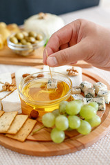 Chef`shand dip the cheese in honey. Cheese mix on a wooden plate decorated with grapes, nuts, salad and olives with cheese knifes .