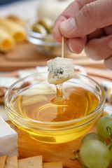 Chef's hand dip the cheese in honey. Cheese mix on a wooden plate decorated with grapes, nuts, salad and olives with cheese knifes 