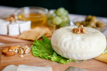 Cheese mix on a wooden plate decorated with grapes, nuts, salad and olives with cheese knifes 