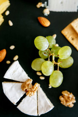 Cheese mix on a black desk, decorated with grapes, nuts, salad and olives with cheese knifes 