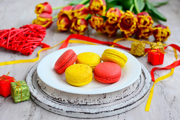 Red and yellow macaroons, ribbons and a bouquet of tulips on a rustic wooden background. Close-up
