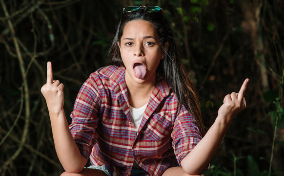 Teenager girl making gun shot gesture. Girl showing middle finger offensive gesture. Negative expression gesturing concept.