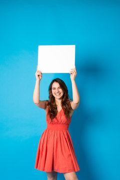 Happy young brunette woman girl in summer clothes toothy smile isolated on blue background studio portrait.Holding white big sign board blank paper overhead. Dentistry, shopping discount sale