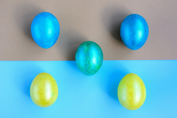 Painted yellow, blue and turquoise eggs lie on light blue and gold paper. Top view. Easter.