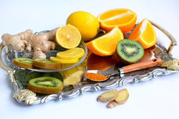 Lemons, oranges, kiwi, ginger and spices on a metal tray on a white background. C