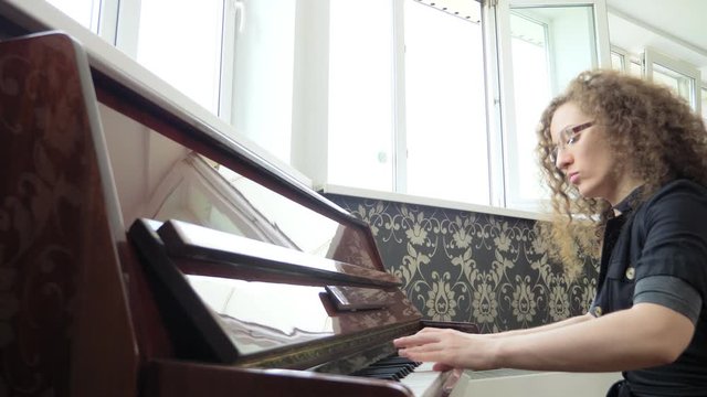 beautiful girl in glasses with curly hair plays the piano