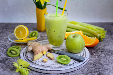 Vitamin smoothie of celery, lemon, kiwi and ginger on a gray background.