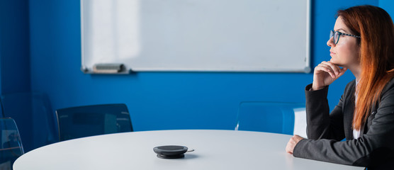 Pensive red-haired office manager in glasses and a suit in an empty conference room. Business woman...