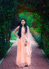 Full length portrait of Young Indian girl standing in front of plant's made gate. Traditional Indian dress .