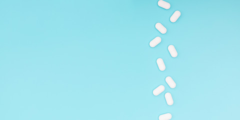 White pills on light blue background. Minimal medical concept. Flat lay, top view, copy space, banner