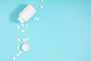 White pills spilled out of white bottle on light blue background. Minimal medical concept. Flat lay, top view, copy space