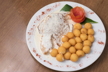 salmon con crema en un plato blanco decorado de tomate con bollitos fritos 