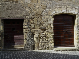 An ancient column, capital and arches appear between two doors in a street in the city of Tarquinia. Italy. 