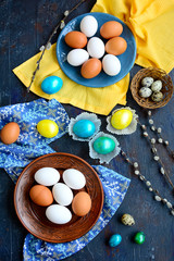 Top view on plates with chicken and quail eggs and bright easter yellow, blue and green eggs on a dark background.