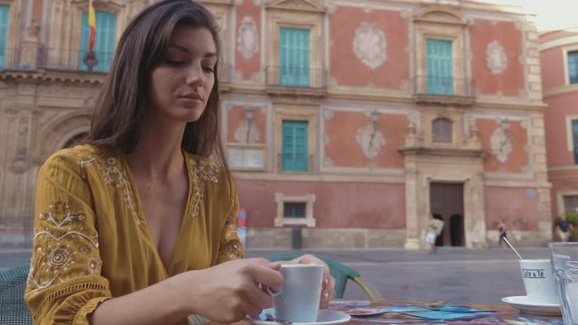 Woman sitting in the old town of Murcia while having a coffee on a terrace with the Murcia Cathedral in the background.