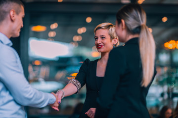 Image of a young attractive businesswoman shaking hands with her client for a deal in front of the office.
