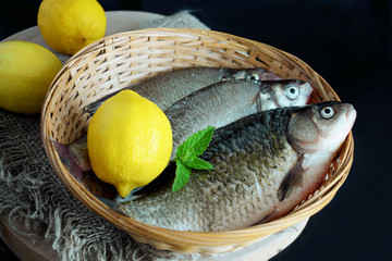 Fresh fish in a wicker basket and lemons on a black background.