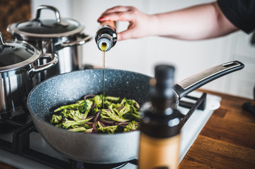 Woman's hand pours olive oil on grilled vegetables in a cast iron grilling pan. Stir fried vegetables in the pan. Fresh sliced vegetables close up. Olive oil on vegetables.