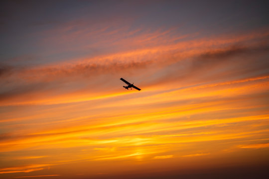 The plane flies across the sunset sky in the evening, bright orange colors, stripes.