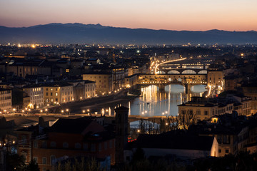 Vista de ciudad de Florencia atravesada por río al anochecer con colinas de fondo