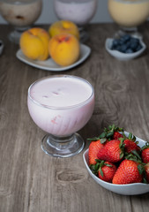 natural strawberry yogurt in a glass cup with fresh fruit in a bowl
