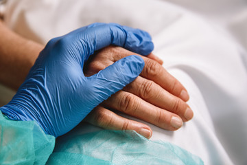 Close up of a doctor hand with blue glove giving support and love to a patient at hospital....