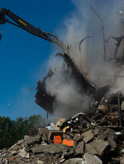 Demolition Excavator tearing down the roof of the building creating a dust cloud.