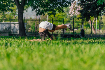 Young sporty handsome man practicing yoga in the park and doing the plow pose..