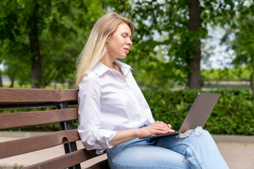 young woman working online through a laptop while sitting on a bench in a country park