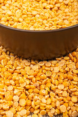 Yellow split peas in a ceramic bowl and grits scattered on a background of coarse-textured burlap. Traditional cereals for making soups and porridge. Close up.