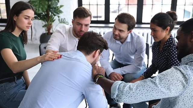 Back rear view desperate young man sharing problems with compassionate mixed race people, sitting together in circle. Diverse patients comforting unhappy guy at team psychological counseling session.