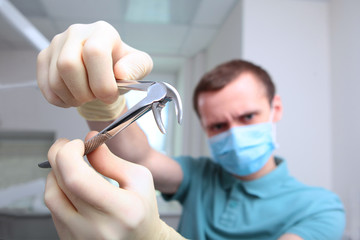 Forceps for removing teeth in the hands of a dentist. Unrecognizable photo. The face is out of focus. Copy of the space.