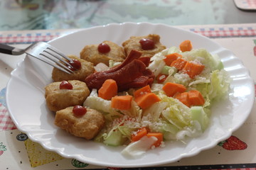 Plato con ensalada con nuggets de pollo con salchicha encima