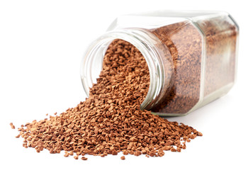 Instant coffee spills out of a glass jar on a white background. Isolated