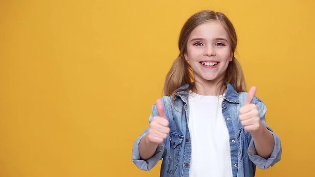 Little fun teen kid girl 12-13 years old in denim jacket white t-shirt posing isolated on yellow background studio People childhood lifestyle concept Smiling showing pointing fingers hand on workspace