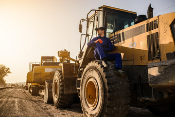 young man contractor builder is sitting on the bulldozer wheel