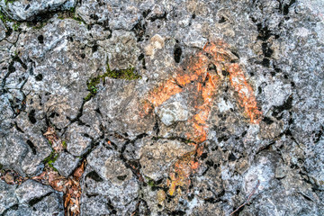 Hiking trail. A grey, rocky road uphill with an orange arrow drawn to indicate the way. Restrained colors of nature