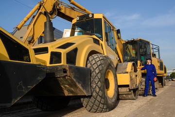 young man contractor builder in blue overalls is looking to the bulldozer wheel.