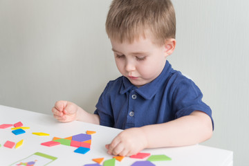 Cute boy plays wooden game tangram. Creative and educational games on quarantine. Copy space