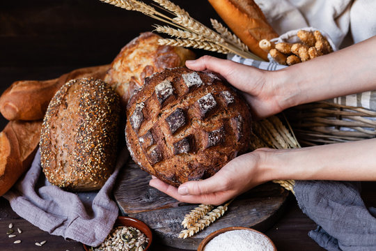 Concept of homemade bread, natural farm products, domestic production. Healthy and tasty organic food. Woman holding round bread freshly baked. Close up,  dark black background