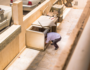 An image of a man in a squat position looking for something inside the broken storage wooden box.