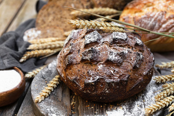 Concept of homemade bread, natural farm products, domestic production. Healthy and tasty organic food. Wheat spica as decor. Closeup, macro, wooden background