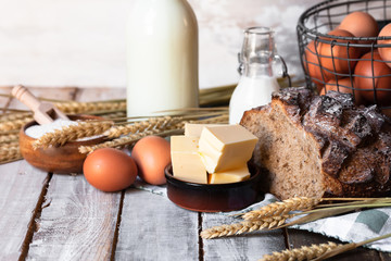 Concept of homemade bread, natural farm products, domestic production. Healthy and tasty organic food. Eggs, butter, bread, milk, flour. Wheat spica as decor. Closeup, wooden background