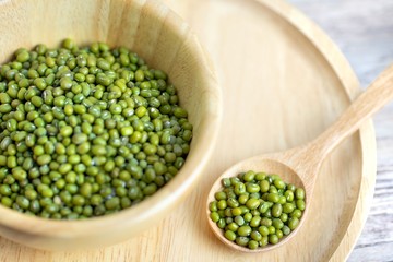 Raw fresh mung beans seed or organic green beans in a wooden bowl and wooden spoon isolated on the wooden plate table background.Healthy food ,Agriculture concept.Copy space.
