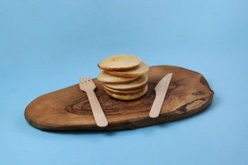 Pancakes folded on a wooden board with wooden appliances on a blue background. There is a place for inscription. Close-up side view.