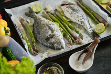 fresh baked dorado fish on a baking sheet with asparagus and lime