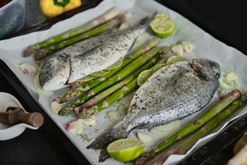 fresh baked dorado fish on a baking sheet with asparagus and lime