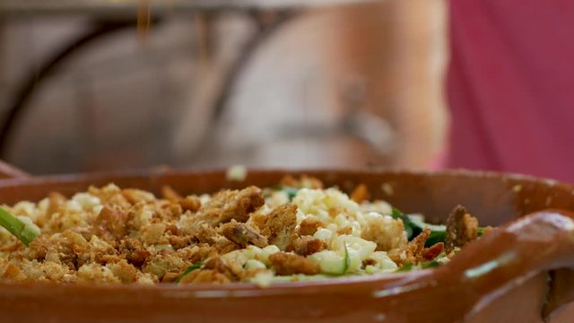 Woman's hand adds small pieces of fried pork into tasty Mexican Corn Salad (Esquites), homemade food preparation